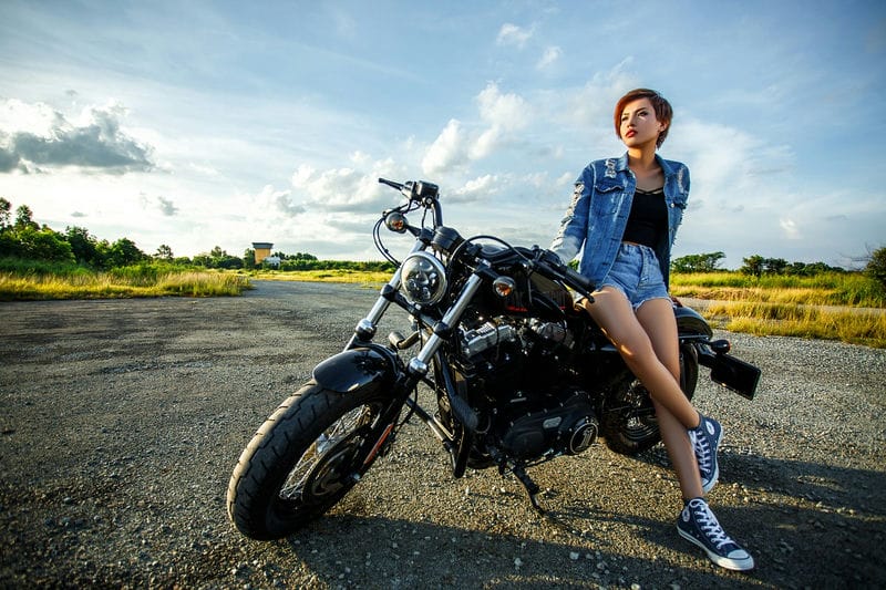 砂利道に停めたバイクに座る女性